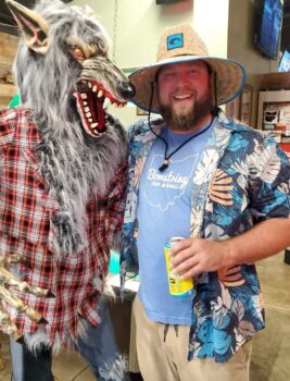 An attendee in a werewolf outfit snarls at the smiling owner in a Hawaiian shirt.