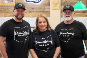 The family poses and smiles together while wearing shirts and hats with the Bowstring logo