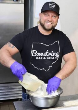 Matt smiles while mixing liquid into dough in a silver bowl.