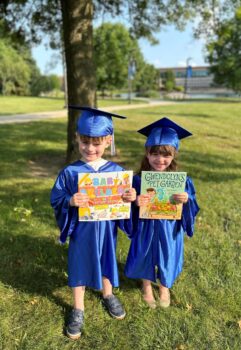 Two 5-year-old twins in blue graduation caps and gowns hold books after graduating from the Imagination Library.