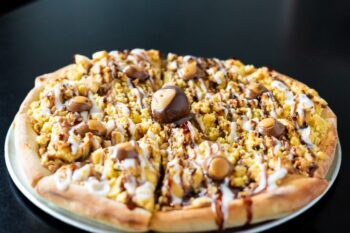 A dessert pizza covered in white icing, chocolate sauce and a Buckeye. 